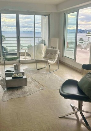 A modern living room with a view of the sea, a white sofa, a black chair, and a small table with a remote control and glasses. - Riviera rooftop - front de mer avec terrasse (Antibes)