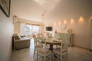 A dining area with a table set for four, a sofa, and a TV mounted on the wall. - Bel Azur (Antibes)