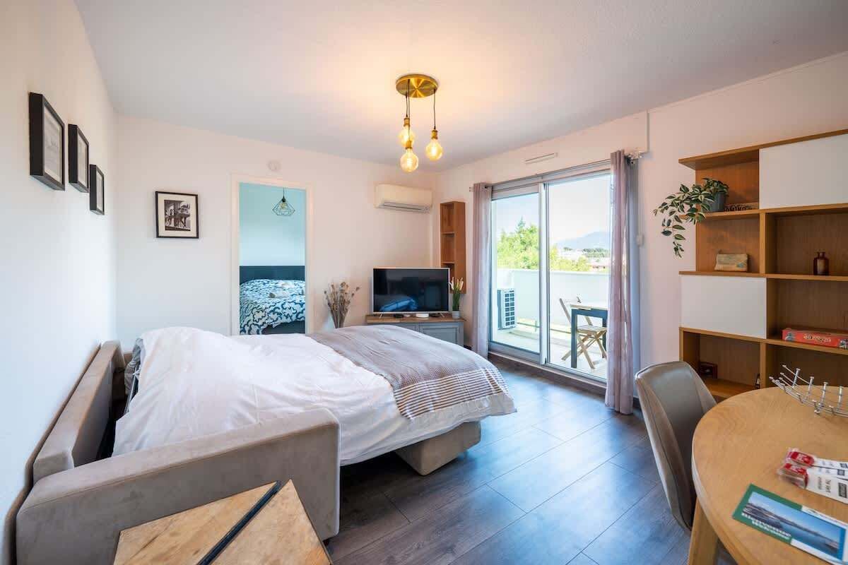 A modern bedroom with a bed, a TV, a balcony with a table, and a bookshelf.