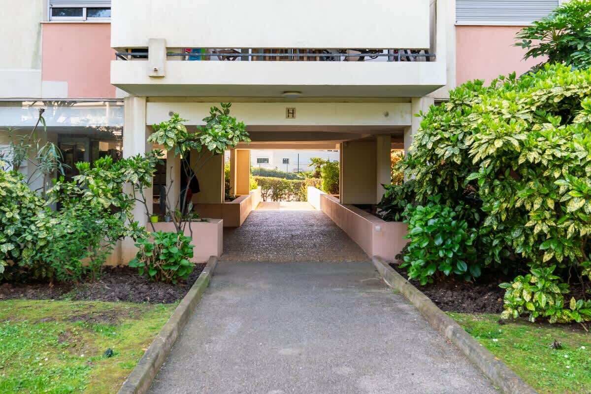 A pathway leading to a building entrance with a covered walkway and greenery on either side.