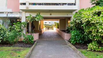 A pathway leading to a building entrance with a covered walkway and greenery on either side.