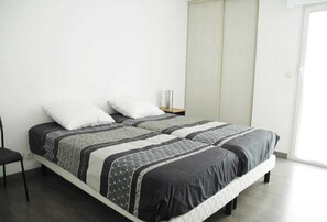 Ein Einzelbett mit gemustertem Überwurf, ein Nachttisch mit Lampe und eine Schiebetür auf der rechten Seite.