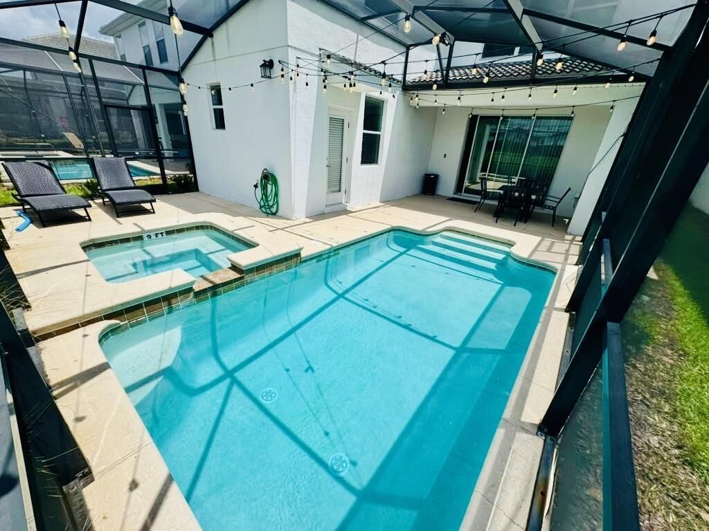 A swimming pool area with two pools, a covered seating area, and a glass-enclosed patio.