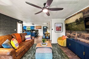 Una sala moderna con un sofá de cuero marrón, un sillón amarillo y un ventilador de techo.