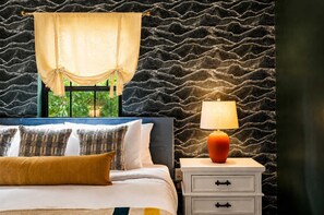 A bedroom with a bed, pillows, a nightstand, a lamp, and a window with a curtain. - Rolling Hills Retreat | Hot Tub • Fire Pit • Sauna (Pigeon Forge)