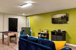 A living room with a foosball table, a sofa, a painting, and a TV on a wall. - Rolling Hills Retreat | Hot Tub • Fire Pit • Sauna (Pigeon Forge)