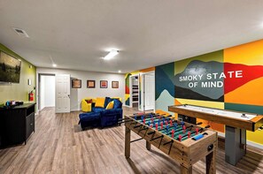 Una habitación con mesa de futbolín, un sofá y una pared decorada con obras de arte coloridas.