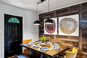 A dining area with a wooden table set for four, a black door with a stained glass window, and two pendant lights. - Rolling Hills Retreat | Hot Tub • Fire Pit • Sauna (Pigeon Forge)