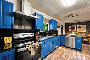 A modern kitchen with blue cabinets, a stainless steel stove, and a wooden floor. - Rolling Hills Retreat | Hot Tub • Fire Pit • Sauna (Pigeon Forge)