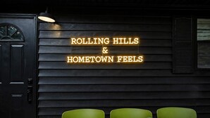 Interior de restaurante con un letrero de neón que dice 'ROLLING HILLS & HOMETOWN FEELS' y una mesa de madera con sillas.
