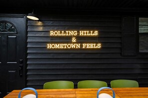 Ein Restaurantinneres mit einem Neon-Schild mit der Aufschrift 'ROLLING HILLS & HOMETOWN FEELS' und einem Holztisch mit Stühlen.