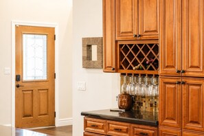 A wooden door with a glass panel, a wine rack with glasses, and a tiled backsplash. - Upsacle Home Putting Green Yard Games Dog Friendly (Scottsdale)