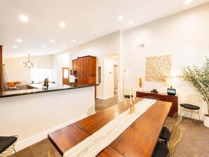 A spacious dining area with a long wooden table, modern chairs, and a kitchen in the background. - Upsacle Home Putting Green Yard Games Dog Friendly (Scottsdale)
