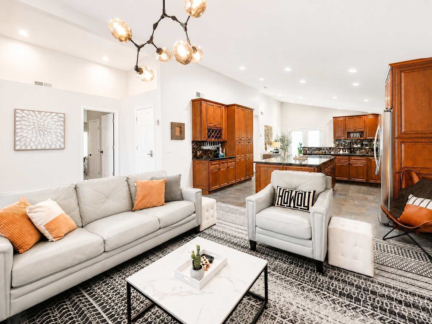 A modern living room with a sofa, armchair, and coffee table, connected to a kitchen with wooden cabinets and a dining area.