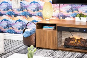 A modern living room with a fireplace, a bookshelf, and a wall with a mountain landscape mural. - Upsacle Home Putting Green Yard Games Dog Friendly (Scottsdale)