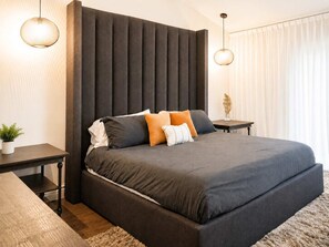 Een moderne slaapkamer met een groot bed, een donker hoofdeinde, nachtkastjes en een potplant.