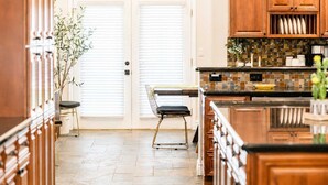 A kitchen with wooden cabinets, a tiled backsplash, and a dining area with a chair and table. - Elevated Beautiful Home Heated Pool Dog Friendly (Scottsdale)