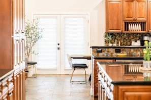 A kitchen with wooden cabinets, a tiled backsplash, and a dining area with a chair and table. - Elevated Beautiful Home Heated Pool Dog Friendly (Scottsdale)