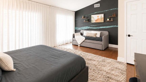 A bedroom with a bed, a grey sofa, a white door, and a wall with artwork. - Elevated Beautiful Home Heated Pool Dog Friendly (Scottsdale)