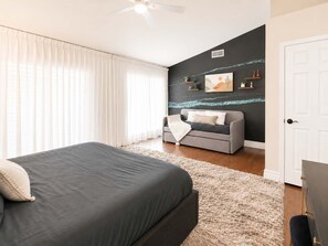 A bedroom with a bed, a grey sofa, a white door, and a wall with artwork. - Upsacle Home Putting Green Yard Games Dog Friendly (Scottsdale)