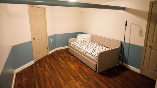 Quarto com cama de canto, piso de madeira, uma porta e parede com faixa azul.