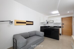 Una sala de estar moderna con un sofá gris, una cocina con armarios blancos y una puerta de madera.