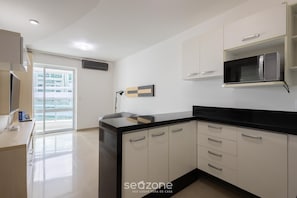 A modern kitchen with white cabinets, a black countertop, and a microwave. - Condo apt w/ Pool in Asa Norte Bhy1704 (Brasília)