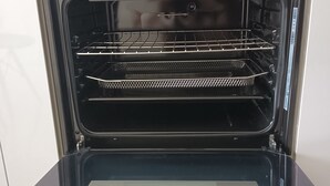 An open oven with a metal rack inside, a control panel with knobs, and a white towel hanging on the door.