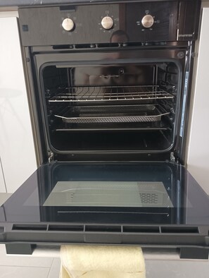 An open oven with a metal rack inside, a control panel with knobs, and a white towel hanging on the door.