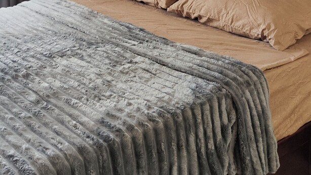A bed with a tufted headboard, two pillows, and a textured blanket.