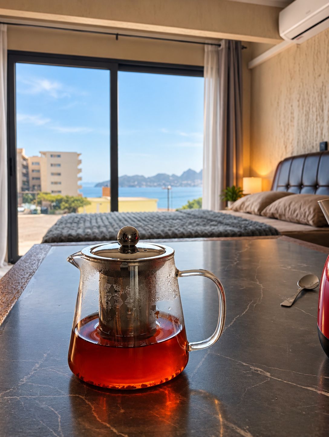 A room with a view of the sea, a bed, and a table with a teapot.