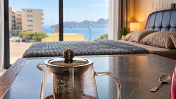 A room with a view of the sea, a bed, and a table with a teapot.