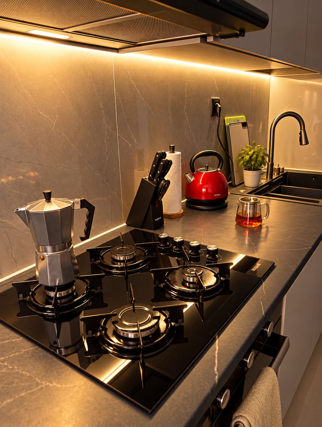 A modern kitchen with a gas stove, a kettle, a sink, and a countertop.