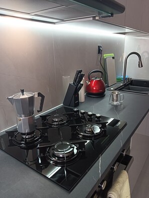 A modern kitchen with a gas stove, kettle, and a sink.