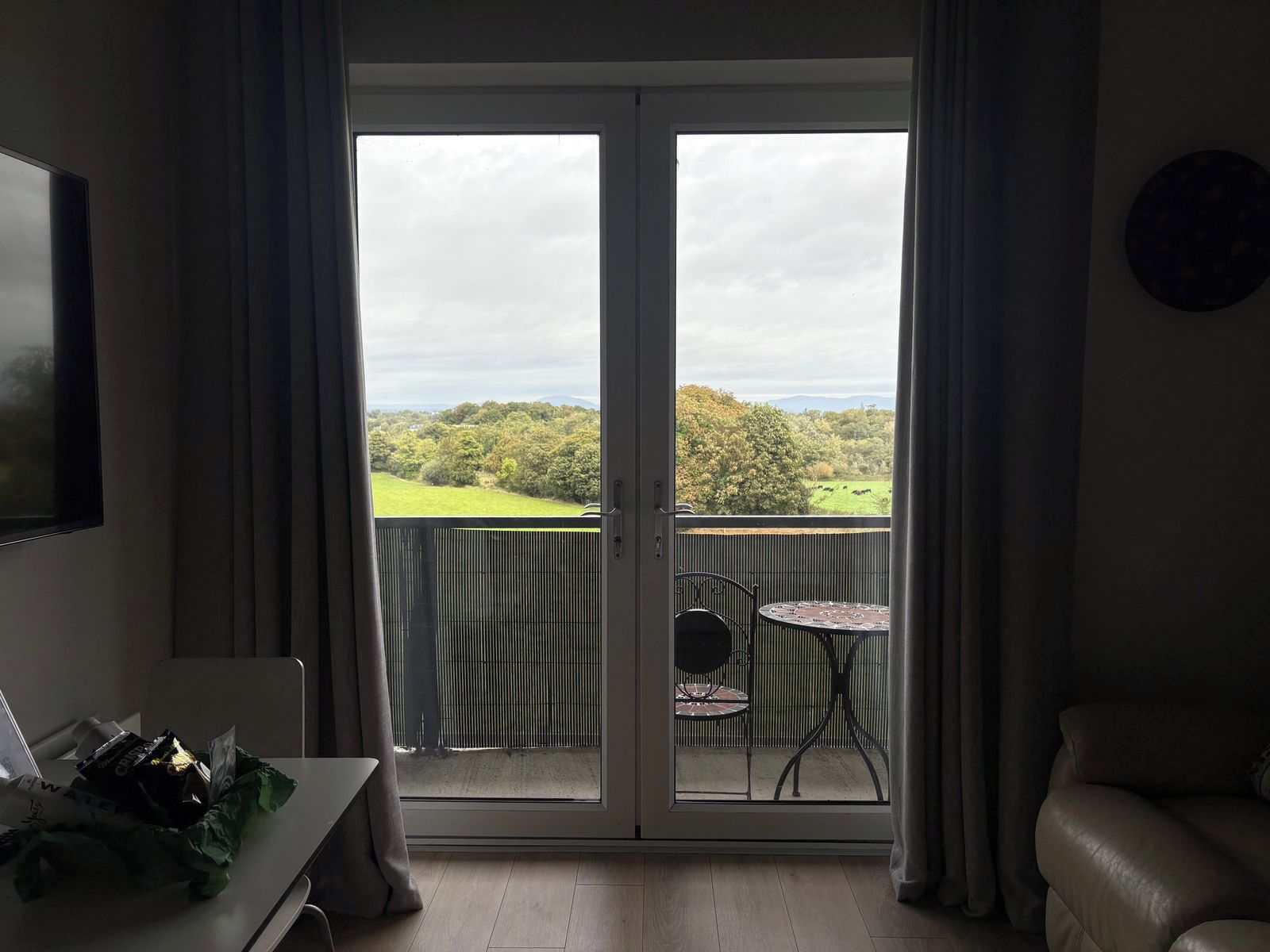 A room with a sliding glass door leading to a balcony with a view of a green landscape and trees.
