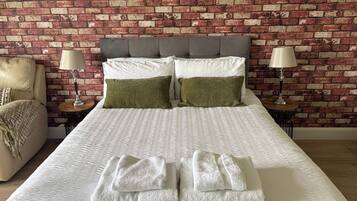 A neatly made bed with a white textured bedspread, two green pillows, and a pair of folded white towels.