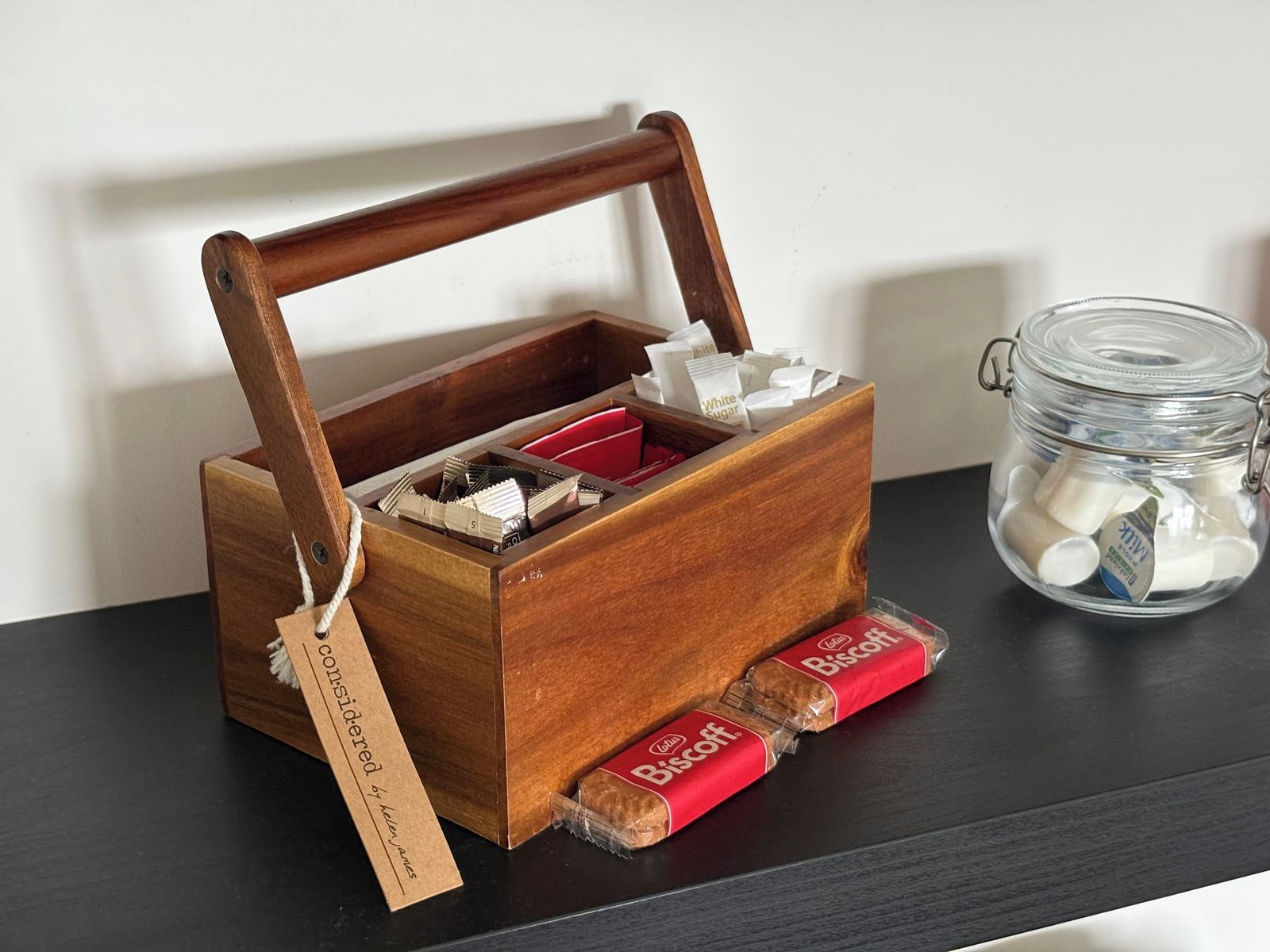 A wooden box with compartments containing sugar packets and a jar of milk.