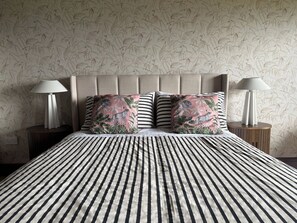 A bed with striped bedding, two pillows with a leopard print and floral design, and two bedside lamps on wooden nightstands. - Family Ensuite, Balcony & Bunks | Boyne Valley (Drogheda)