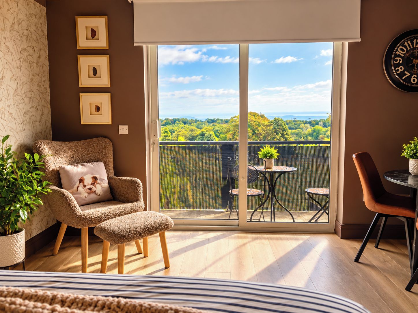 A room with a sofa, a chair, a small table with a plant, and a balcony with a view of the landscape.