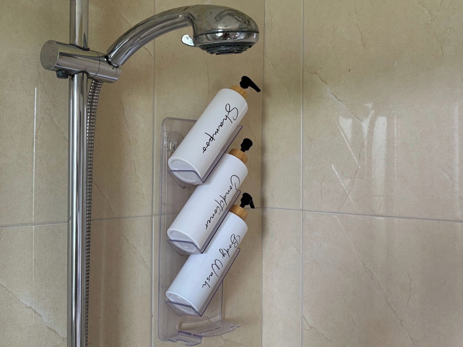 Een douchegedeelte met een chromen kraan en drie flessen shampoo in een transparante houder.