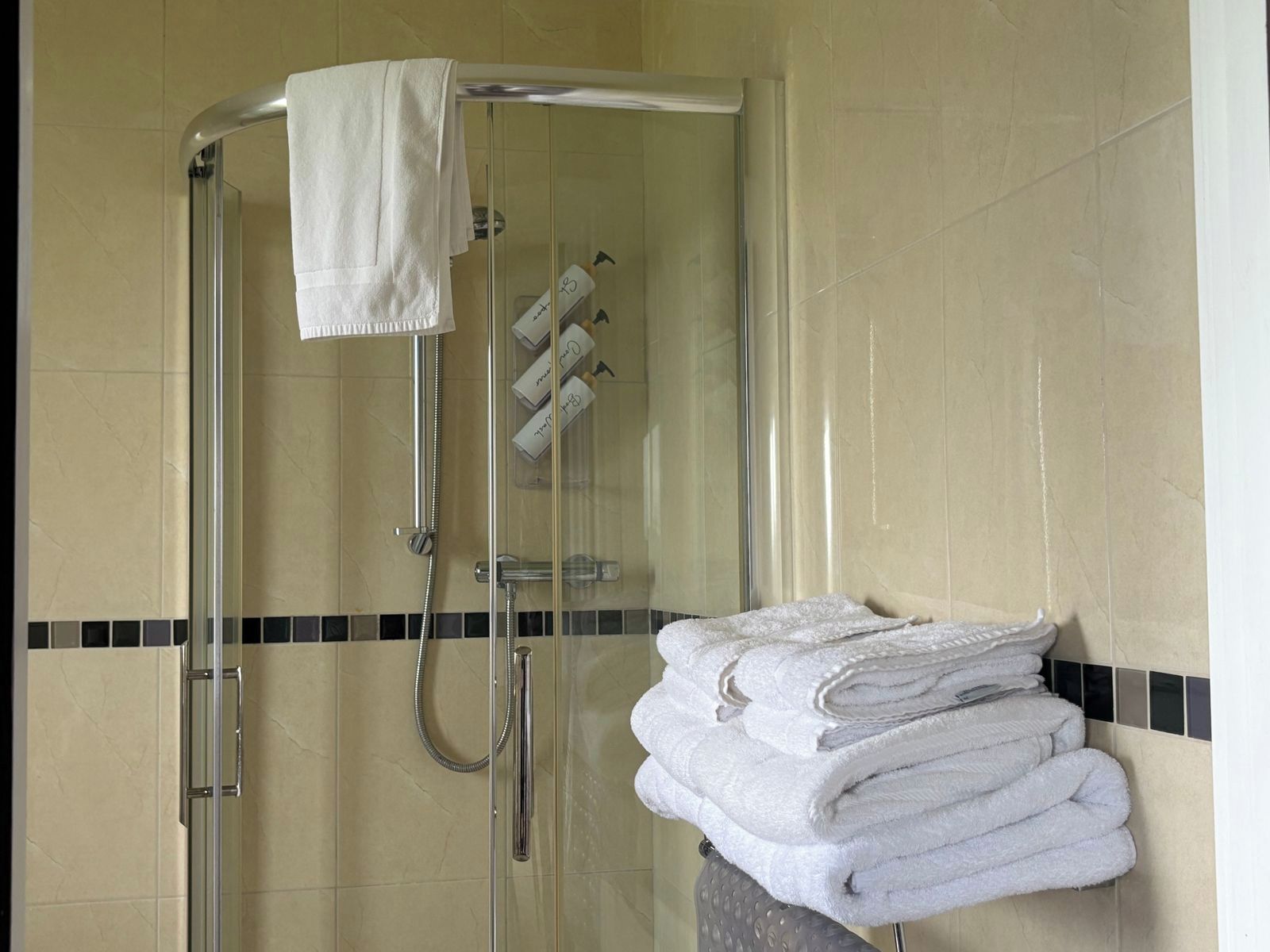 A glass-enclosed shower area with a towel rack holding folded towels, a glass shower door, and a tiled wall.