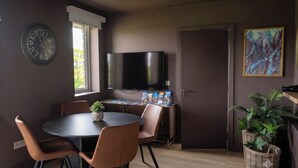 A modern dining area with a round table, chairs, a clock, a flat-screen TV, and a door. - Family Ensuite, Balcony & Bunks | Boyne Valley (Drogheda)