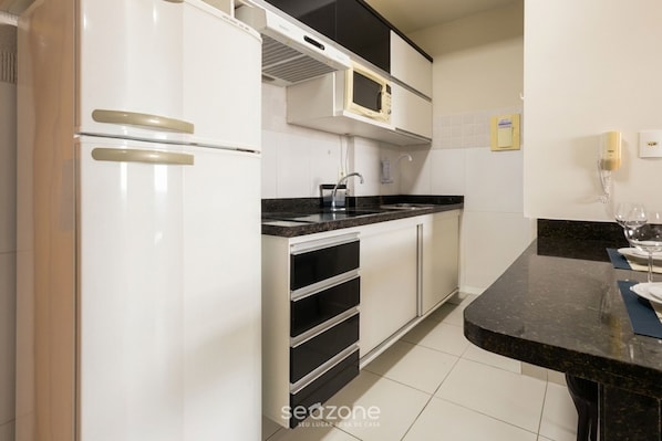A kitchen with white cabinets, a black countertop, and a microwave.