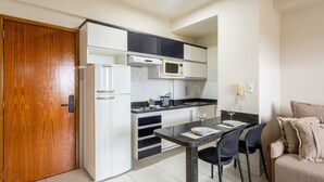 A compact kitchen with white cabinets, a microwave, and a dining area with a table and chairs. - Studio in Condo w/ Pool in Setor Bueno Bli2903 (Goiânia)