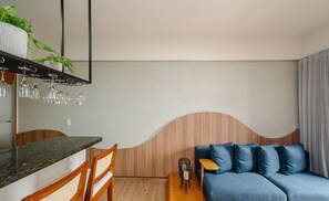 A modern room with a wooden headboard, a blue sofa, a wooden dining table, and a bar area with glasses.