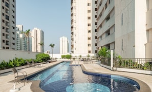 A swimming pool with lounge chairs, surrounded by high-rise buildings and greenery.