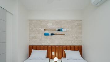 Un dormitorio con pared de ladrillo, dos camas con ropa de cama blanca y dos palas colgadas en la pared.