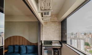 A compact living space with a built-in kitchen, a wooden headboard, and a city view.