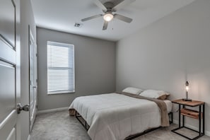 A bedroom with a bed, a bedside table with a lamp, a ceiling fan, and a window with blinds. - Delightful 3-bedroom townhome in peaceful Edmond. Right off the I-35 (Edmond)