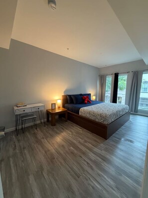 A modern bedroom with a large bed, bedside tables, a desk, and a view of the outdoors.